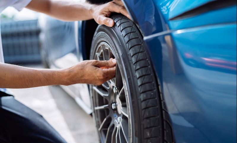 A man is checking the valve on a tire of a blue car.